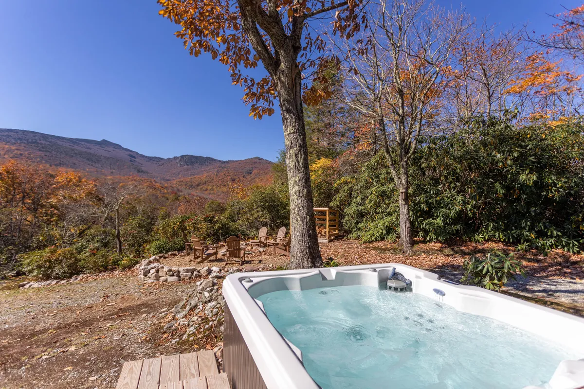 A serene hot tub sits on the deck, overlooking a majestic mountain range and glowing fall foliage. The seating area nearby hints at gathering spots for friends and family, while the open view invites both sunrise coffee and sunset stargazing.