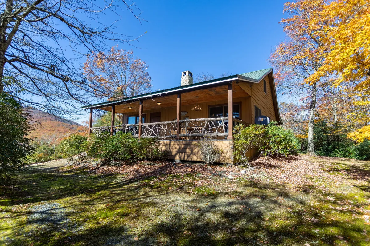A wooden porch framed by colorful autumn foliage and the front entrance of the house. The image suggests peaceful mornings, nature walks, and tranquil evenings, all within easy reach of the outdoors.