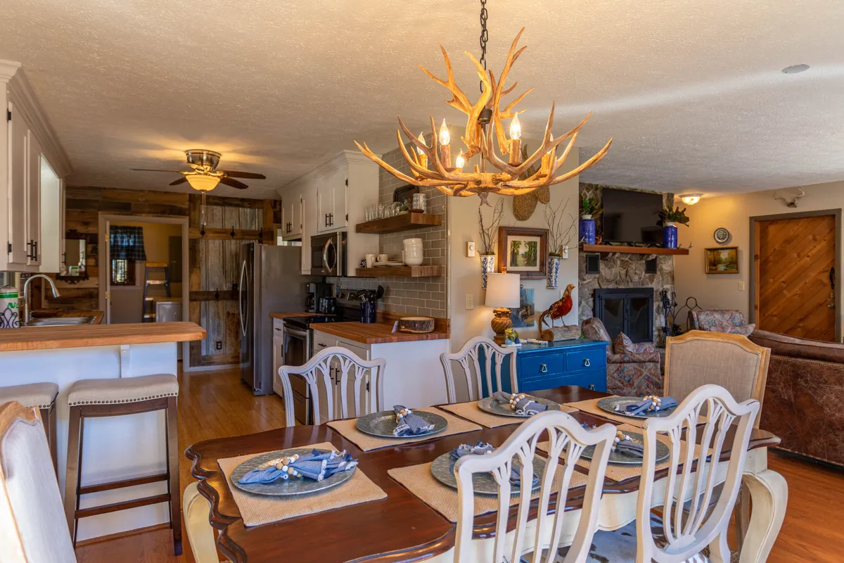 A dining area set for a meal, complete with a rustic chandelier, a welcoming stone fireplace, and a blue sideboard that adds a pop of color. The scene is designed for family meals, social gatherings, and warm, inviting evenings.