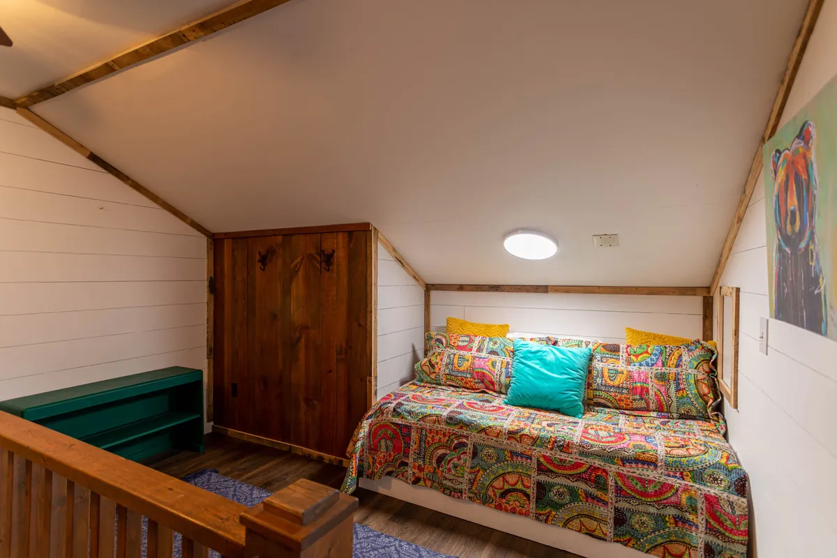 A cheerful bedroom with colorful bedding, wooden furniture, and lively artwork on the walls, offering a sense of warmth and personality. The space feels both welcoming and flexible, suitable for families or friends sharing a room.