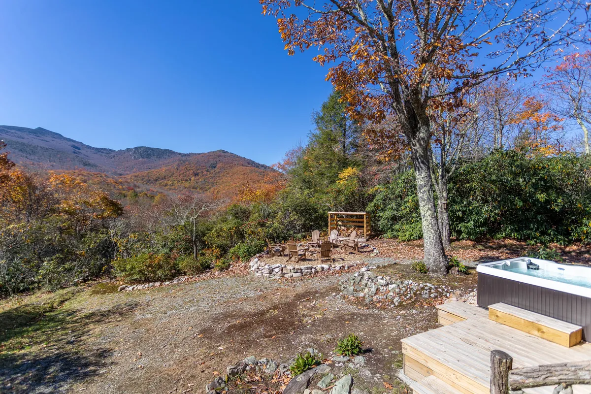 This image captures the outdoor hot tub and fire pit seating area, surrounded by autumn foliage and offering sweeping mountain views. Adirondack chairs are arranged around the fire pit, perfect for gatherings and relaxation. The tranquil setting emphasizes the peaceful and rejuvenating atmosphere of mountain living.