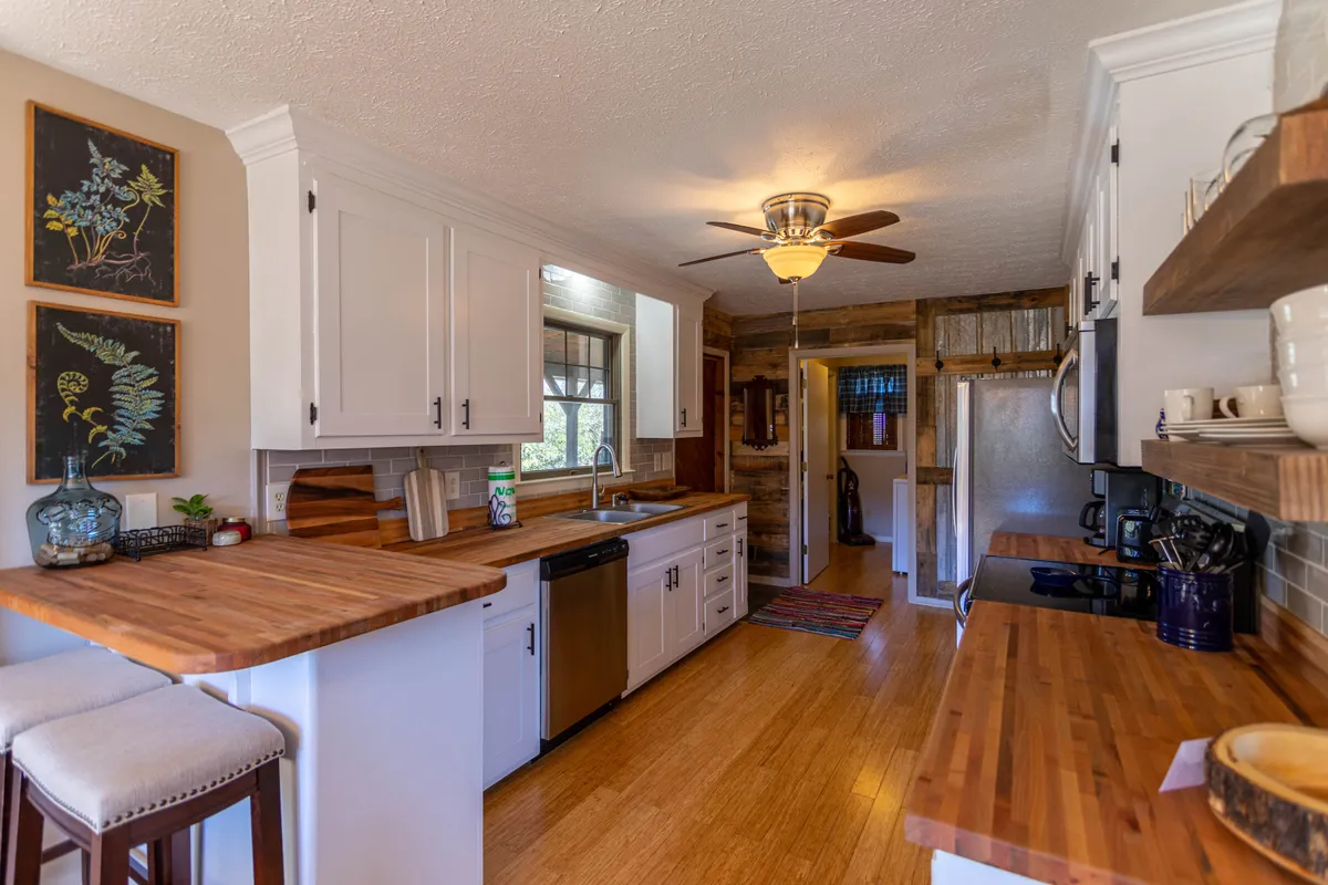 A well-equipped kitchen with gleaming stainless steel appliances, wooden butcher-block countertops, and a kitchen island with seating, accented by tasteful framed botanical art. The setup is perfect for preparing hearty meals and casual breakfasts.
