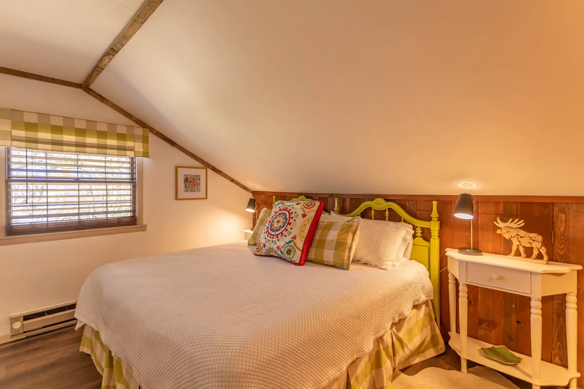 A cozy bedroom with a bright yellow bed frame, colorful pillows, wooden wall accents, and a unique bedside lamp. The cheerful design and inviting bed make the space appealing for children or solo travelers.