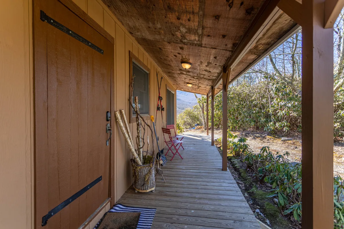 A close-up of the front door and porch area, featuring comfortable red chairs and decorative touches. The scene invites socializing and relaxation, emphasizing the peaceful ambiance and breathtaking views that can be enjoyed at dusk or dawn.