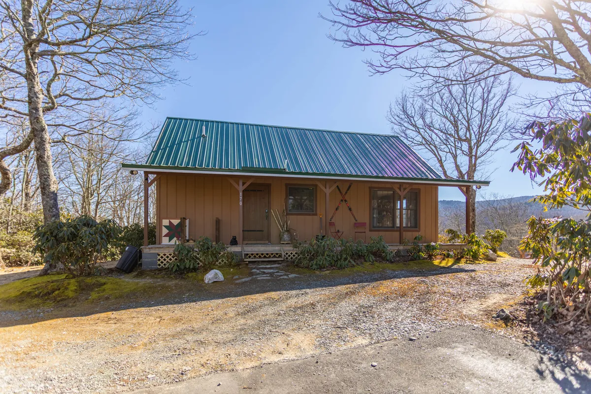 This image captures the front of Heaven’s View, featuring the house with its green metal roof, inviting front door, and attractive landscaping. The setting highlights the welcoming approach and the spacious outdoor surroundings, ideal for guests and their pets to enjoy.