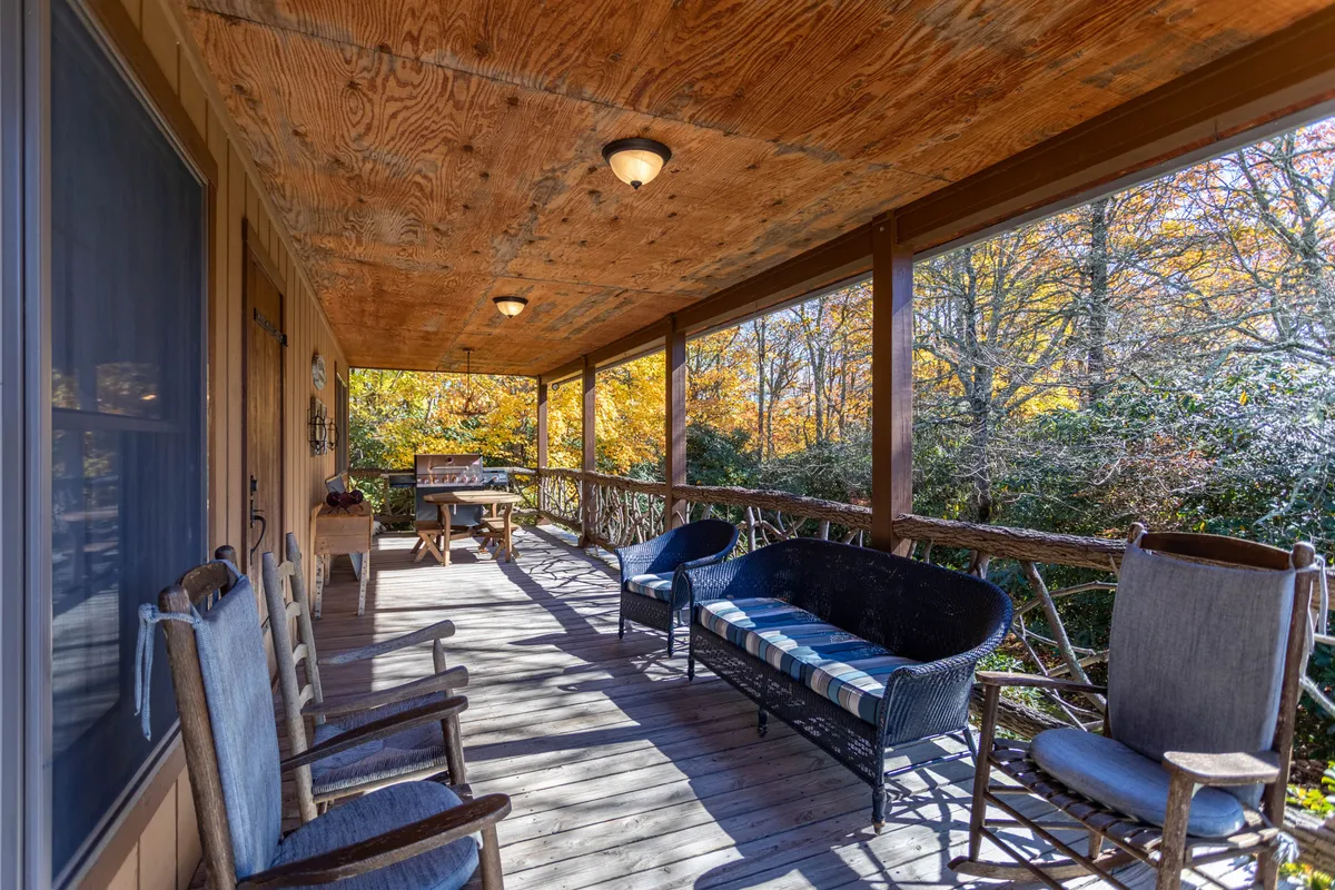 A cozy porch scene with rocking chairs, a woven couch, a wooden table, and surrounding trees. The space is designed for relaxation and socializing outdoors, providing a comfortable spot for guests—and their pets—to enjoy nature.