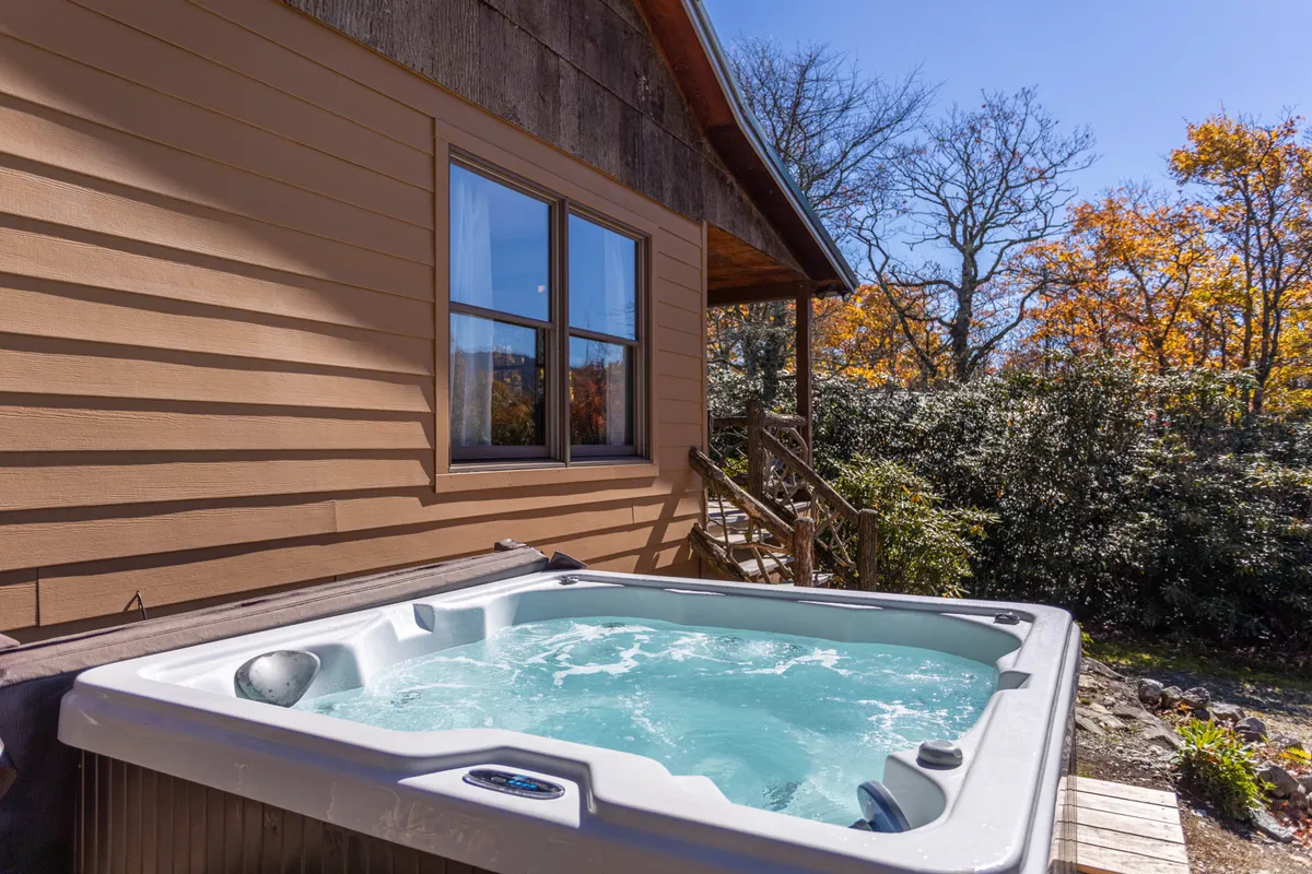 The tranquil outdoor hot tub surrounded by trees and the cabin exterior offers a rejuvenating spot for relaxation with a picturesque natural backdrop.