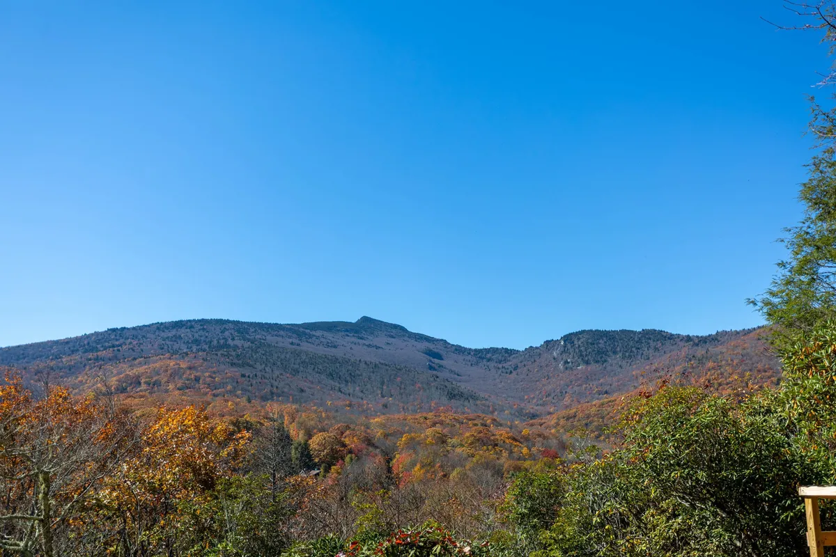 This image showcases breathtaking mountain views with vibrant autumn foliage and a clear blue sky, perfectly representing the natural beauty and outdoor adventure available near Blue Ridge Parkway and Grandfather Mountain.