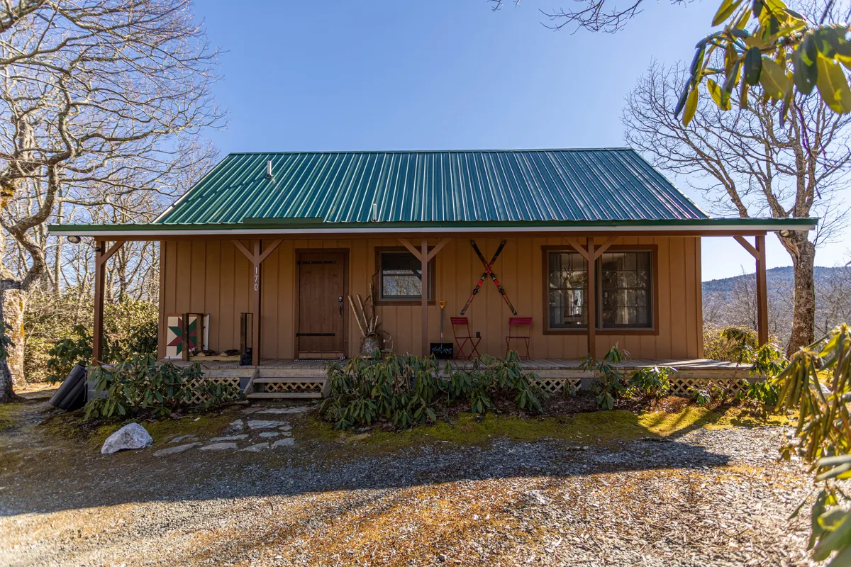 A charming exterior shot of the retreat’s wooden door and green metal roof, featuring a front porch decorated with welcoming accents. The porch is ideal for relaxing with friends while taking in the natural surroundings. Decorative items on the walls and the rustic feel set the stage for outdoor leisure and connection to nature.