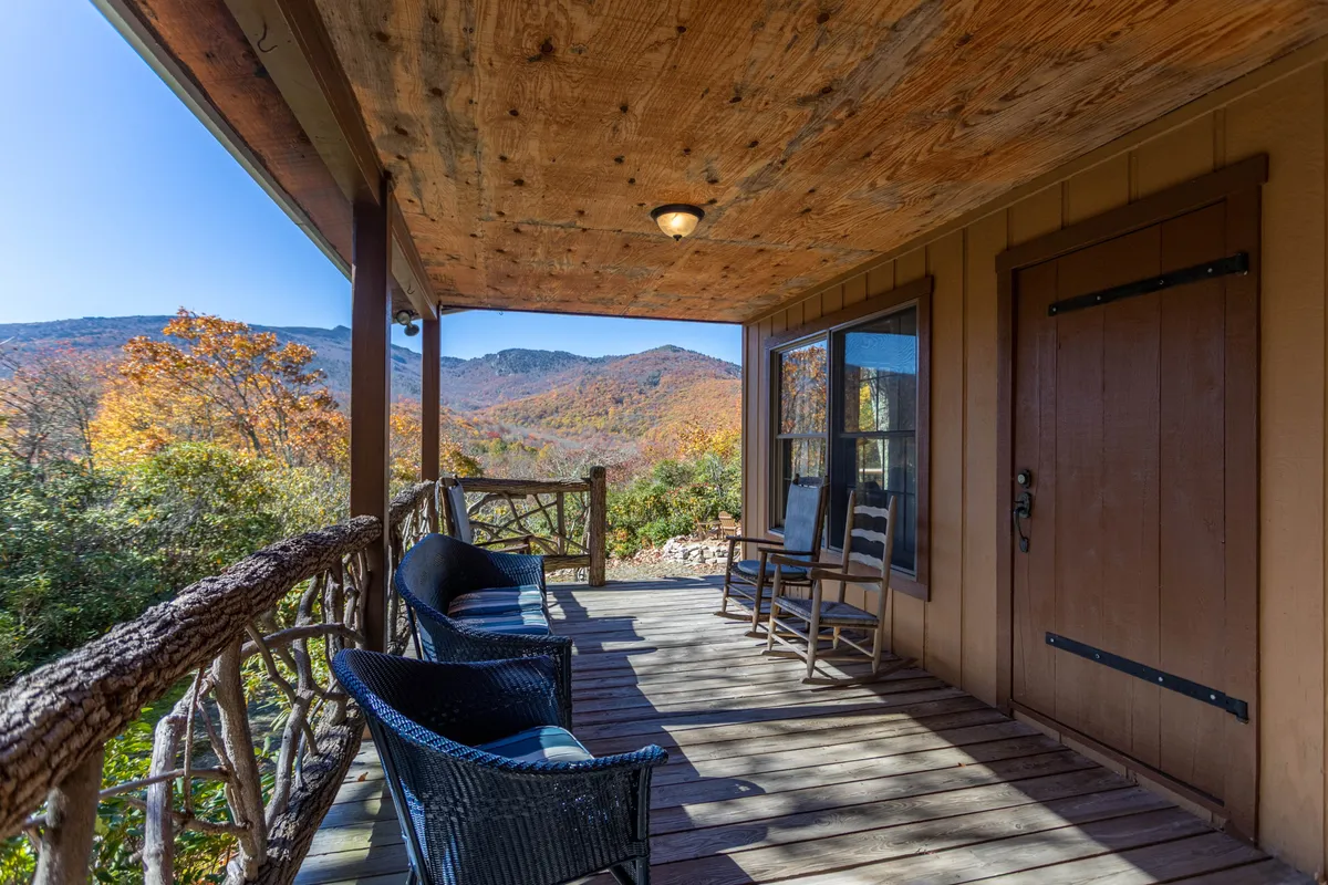This image features a wooden porch furnished with rocking and woven chairs, all set against a backdrop of sweeping mountain views. The tranquil setting is ideal for relaxing and unwinding while enjoying nature, with the porch inviting guests to meditate, read, or simply take in the breathtaking landscape.